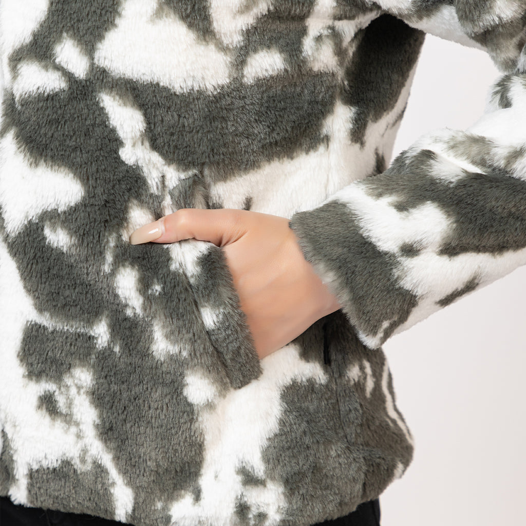 Close-up of a person wearing a gray and white patterned sweater with a hand visible. Amoldo