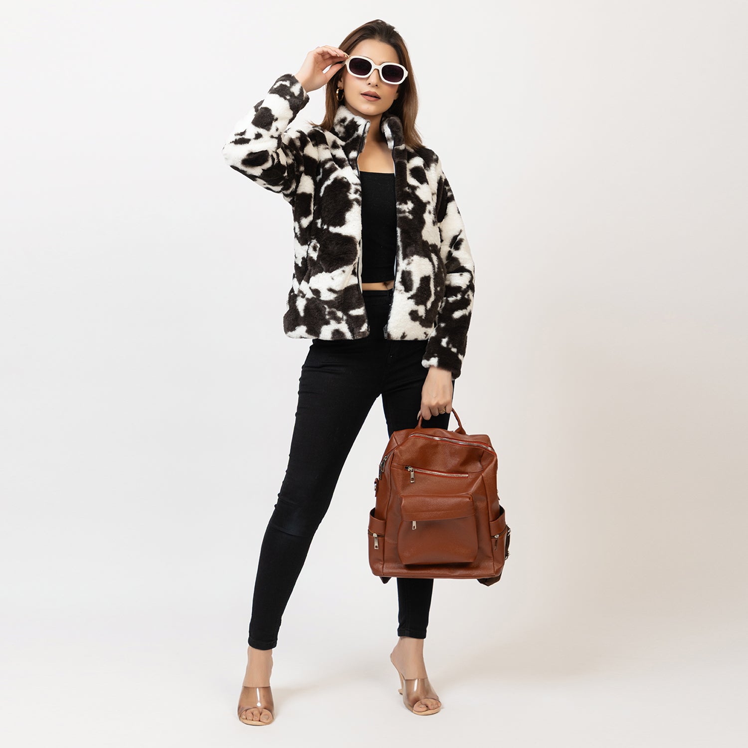 Woman wearing a black and white patterned jacket with a brown leather backpack on a white background Amoldo 